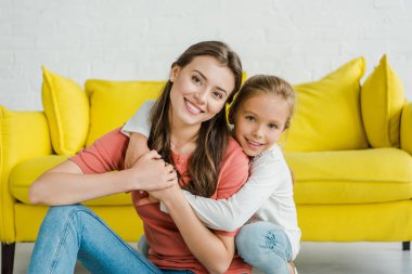 Mutlu çocuk gülümserken neşeli bebek bakıcısını kucaklıyor oturma odasında. 