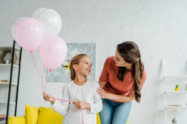 Neşeli bebek bakıcısı pembe balonlar tutan mutlu çocuğa bakıyor. 