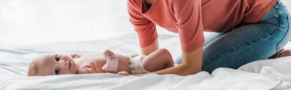 ベッドの上に寝そべっている可愛い赤ちゃんに触れる母親のパノラマ写真 — ストック写真