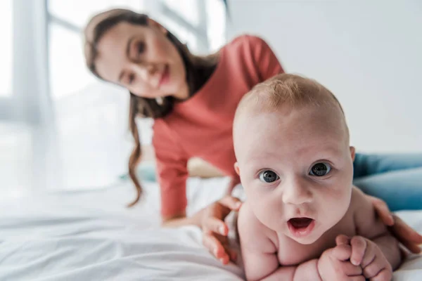 選択的フォーカスかわいい赤ちゃんは寝室で幸せな母親の近くにカメラを見て — ストック写真