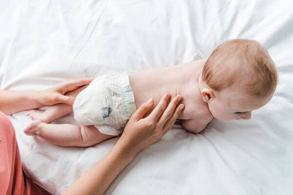 Вид сверху на мать, трогающую маленькую дочь в пеленке
