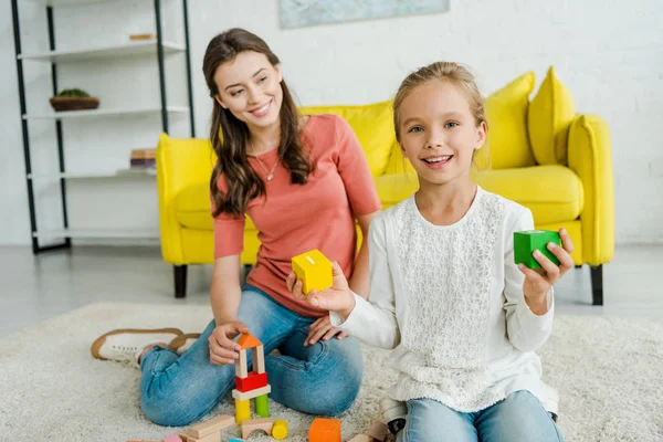 Foco Seletivo Criança Feliz Segurando Blocos Brinquedos Perto Babá Alegre — Fotografia de Stock