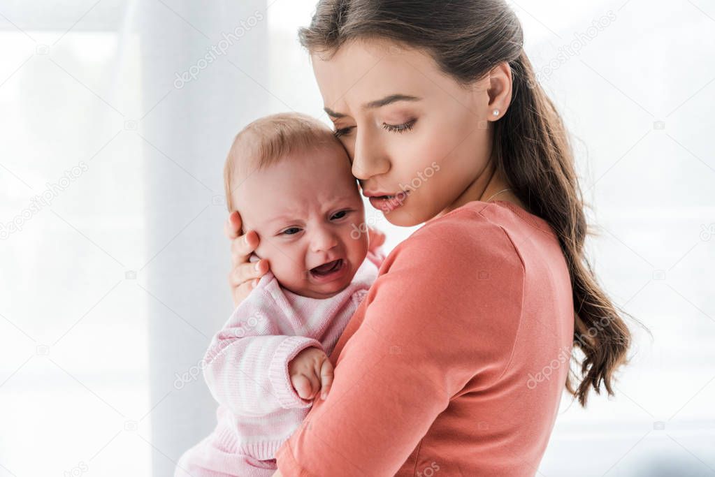 attractive mother holding in arms crying infant at home 