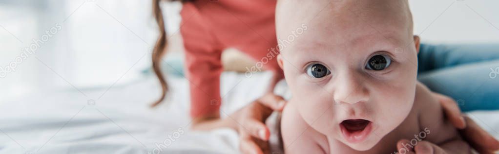 panoramic shot of woman touching baby daughter lying on bed 