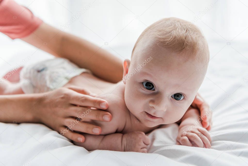 cropped view of mother doing massage to cute infant daughter lying on bed at home 