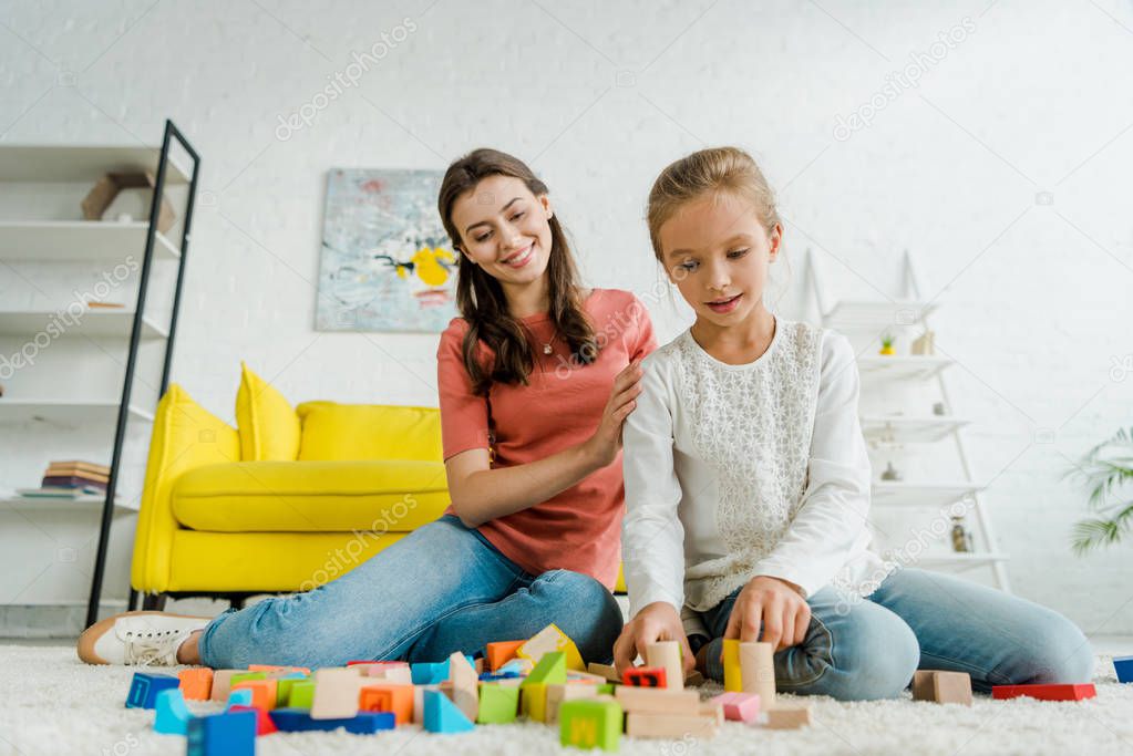 selective focus of kid playing with building bricks near babysitter 