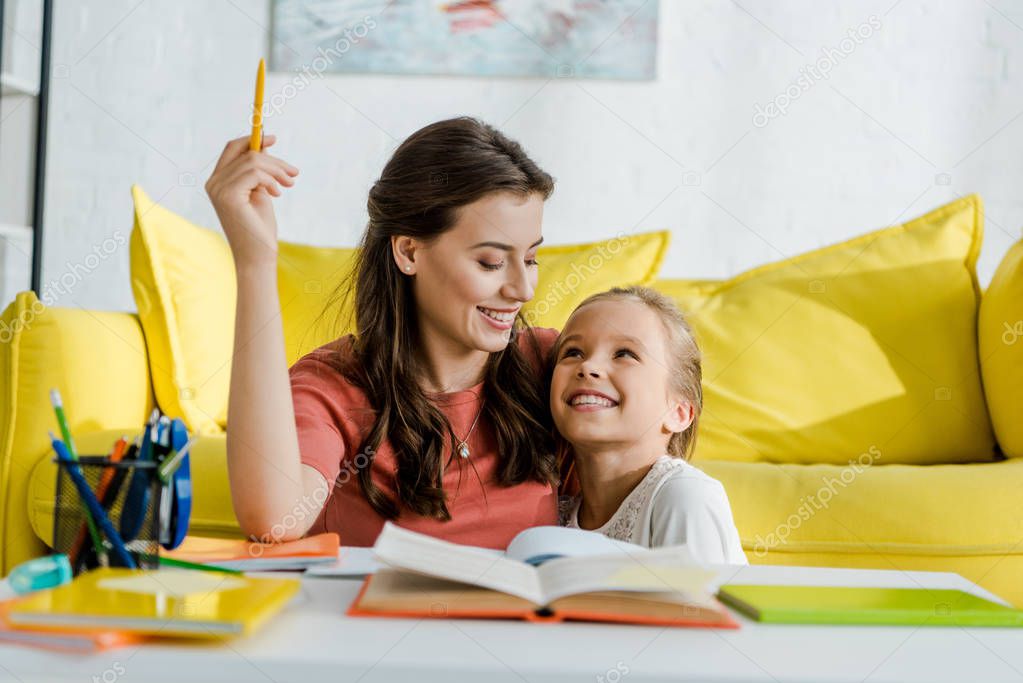 selective focus of happy kid looking at babysitter holding pen near notebooks in living room 