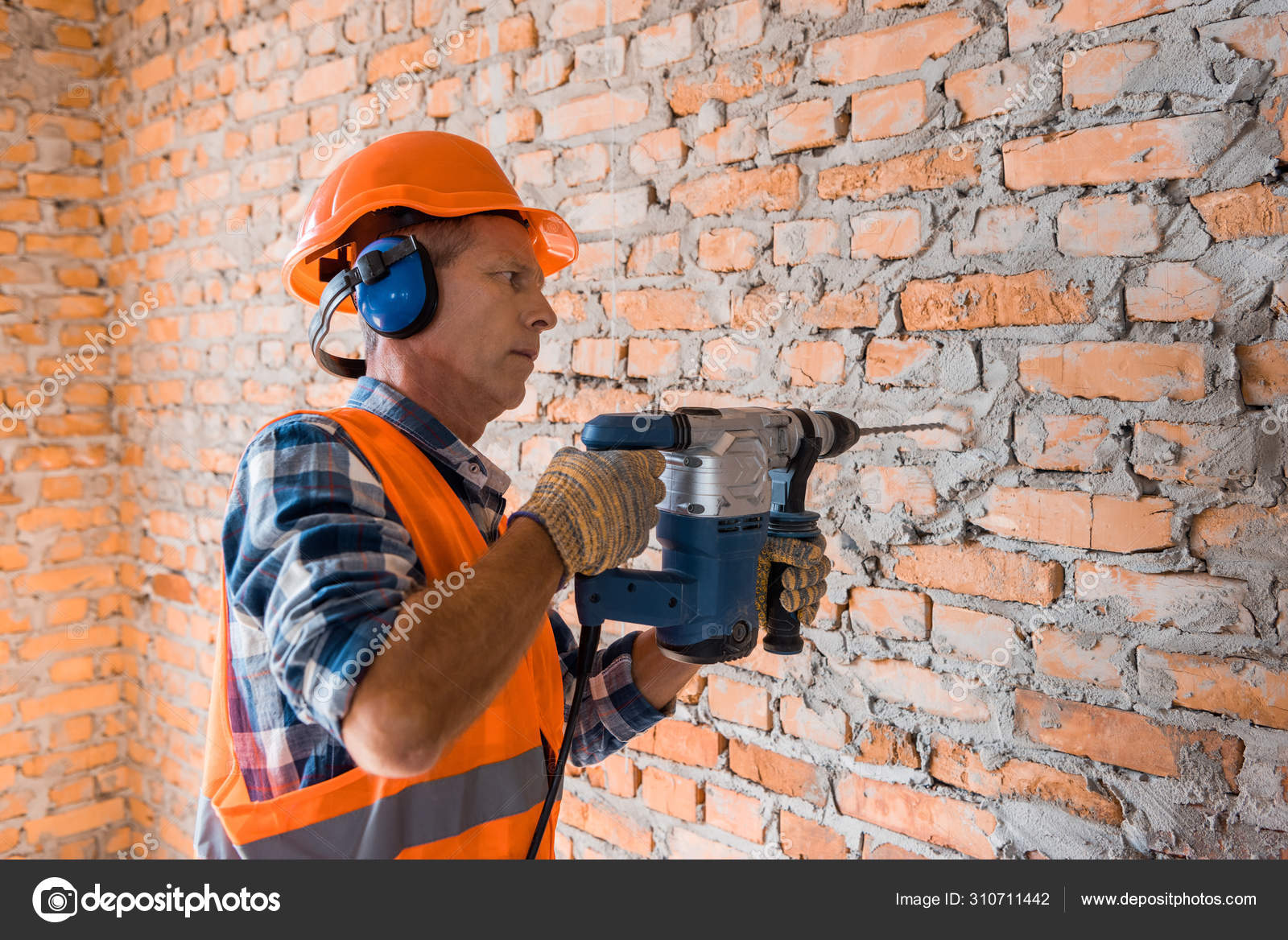 Mature Builder Helmet Using Hammer Drill Brick Wall Stock Photo by