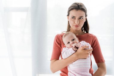 Kafası karışmış bir anne kucağında sevimli bir kız çocuğunu evde tutuyor. 