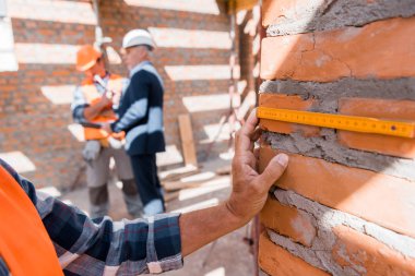cropped view of mature man measuring brick wall near coworker and businessman  clipart