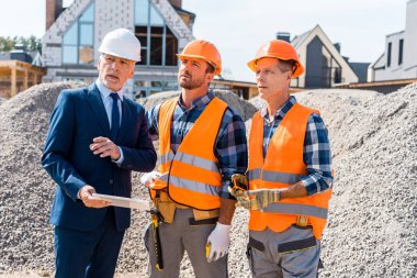 constructors in helmets standing near businessman with digital tablet  clipart