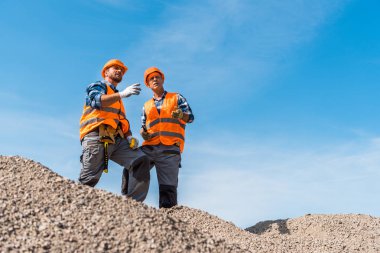Turuncu miğferli iş arkadaşlarının seçici odak noktası gökyüzüne karşı duran kayalar. 