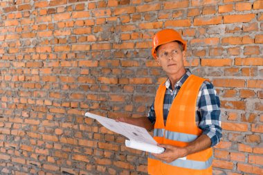 handsome mature man holding blueprint near brick wall  clipart
