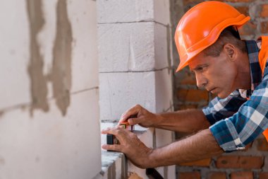 selective focus of middle aged constructor in helmet measuring concrete wall  clipart