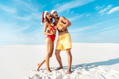 sexy and smiling girlfriend and boyfriend holding gifts on beach in Maldives  clipart