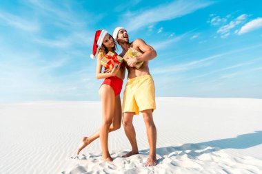 sexy and smiling girlfriend and boyfriend holding gifts on beach in Maldives  clipart