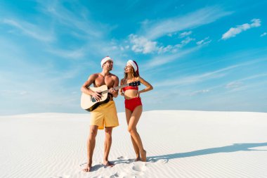 sexy girlfriend and boyfriend playing acoustic guitar on beach in Maldives  clipart