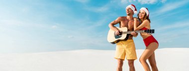panoramic shot of sexy girlfriend and boyfriend playing acoustic guitar on beach in Maldives  clipart