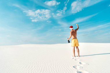 Maldivler sahilinde elinde cam ve şişe tutan Noel Baba şapkalı seksi bir adam. 