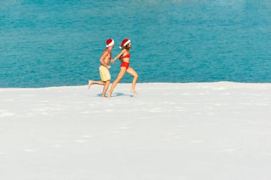 Maldivler 'de plajda koşan Noel Baba şapkalı seksi kız ve erkek arkadaş 