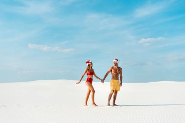 Noel Baba şapkalı seksi kız ve erkek arkadaş el ele tutuşup Maldivler 'de sahilde yürüyor. 