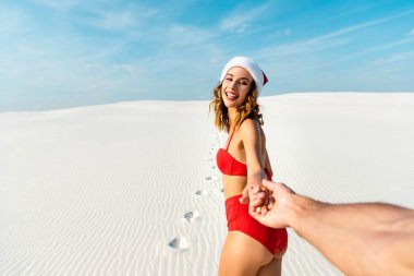 Erkek arkadaşın, Maldivler 'deki kumsalda Noel Baba şapkalı seksi kız arkadaşının el ele tutuşması görüntüsü. 