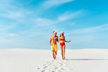 sexy girlfriend and boyfriend in santa hats running on beach in Maldives  clipart