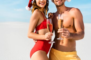 cropped view of sexy girlfriend and boyfriend holding champagne glasses and hugging on beach in Maldives  clipart