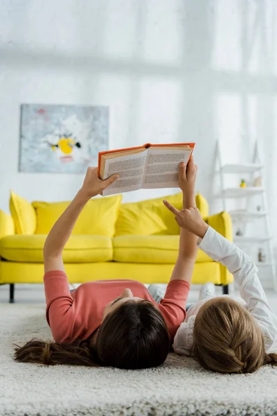 Dziecko Wskazujące Palcem Książkę Leżąc Dywanie Opiekunką — Zdjęcie stockowe