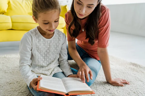 Kind Lezen Boek Terwijl Zitten Tapijt Met Mooie Babysitter — Stockfoto