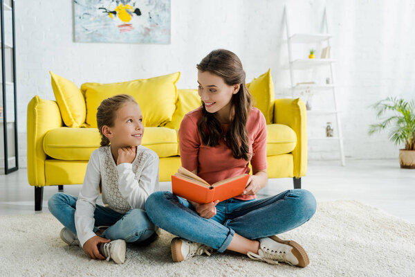 happy kid sitting on carpet with babysitter holding book 