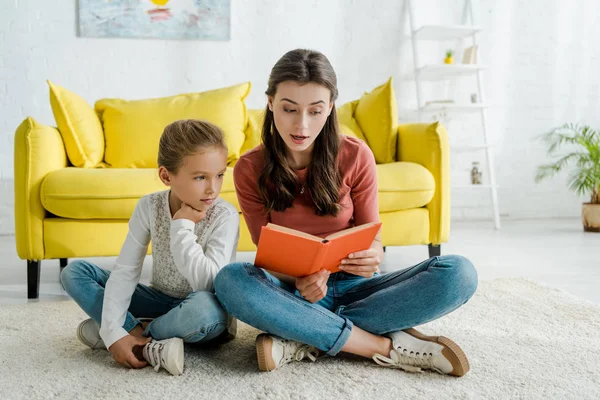 Niedliche Kind Sitzt Auf Teppich Mit Babysitter Buch Lesen — Stockfoto