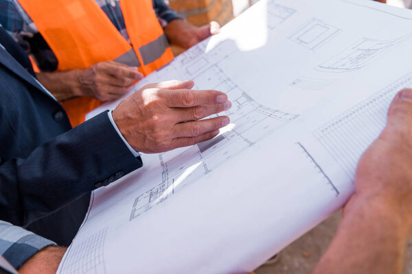 cropped view of businessman gesturing near blueprint and constructors 