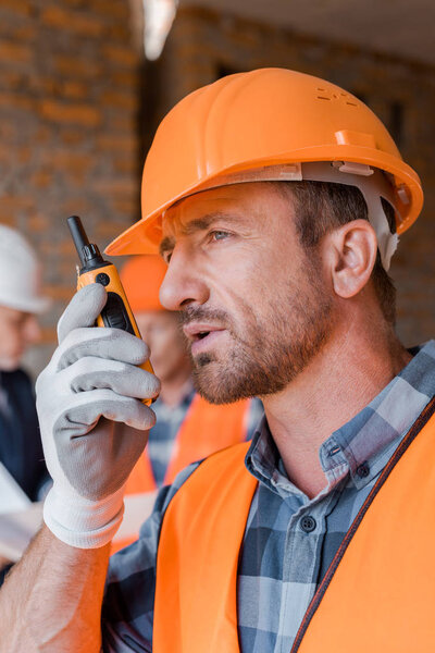 selective focus of handsome constructor talking while holding walkie talkie 
