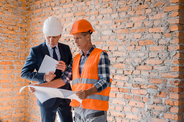 architect holding blueprint near businessman with digital tablet 