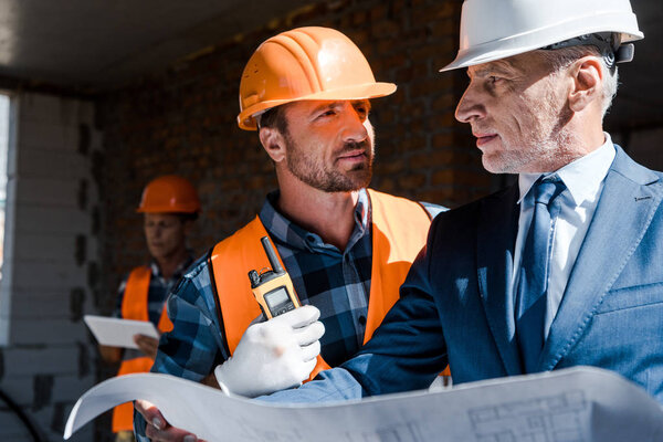 selective focus of businessman holding blueprint near constructor 