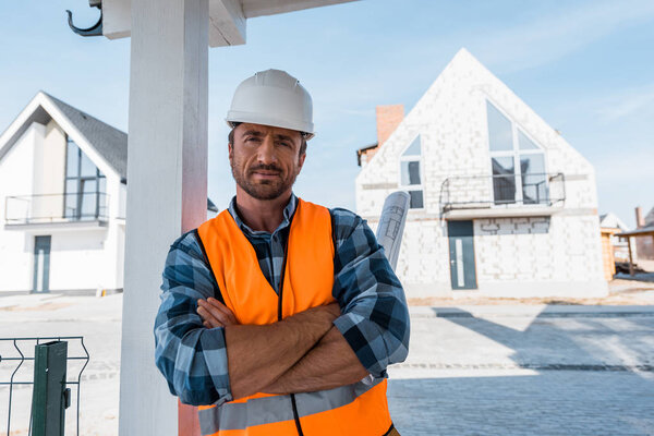 Красивый мужчина со скрещенными руками стоит рядом с домами
 