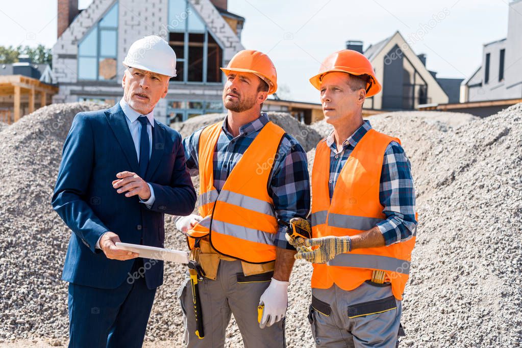 constructors in helmets standing near businessman with digital tablet 