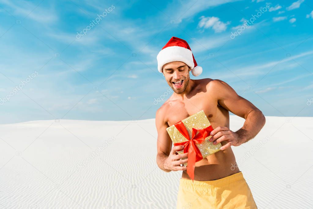 handsome and sexy man in santa hat holding gift on beach in Maldives 