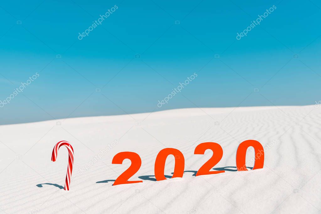 2020 numbers and candy cane on white sand on beach in Maldives
