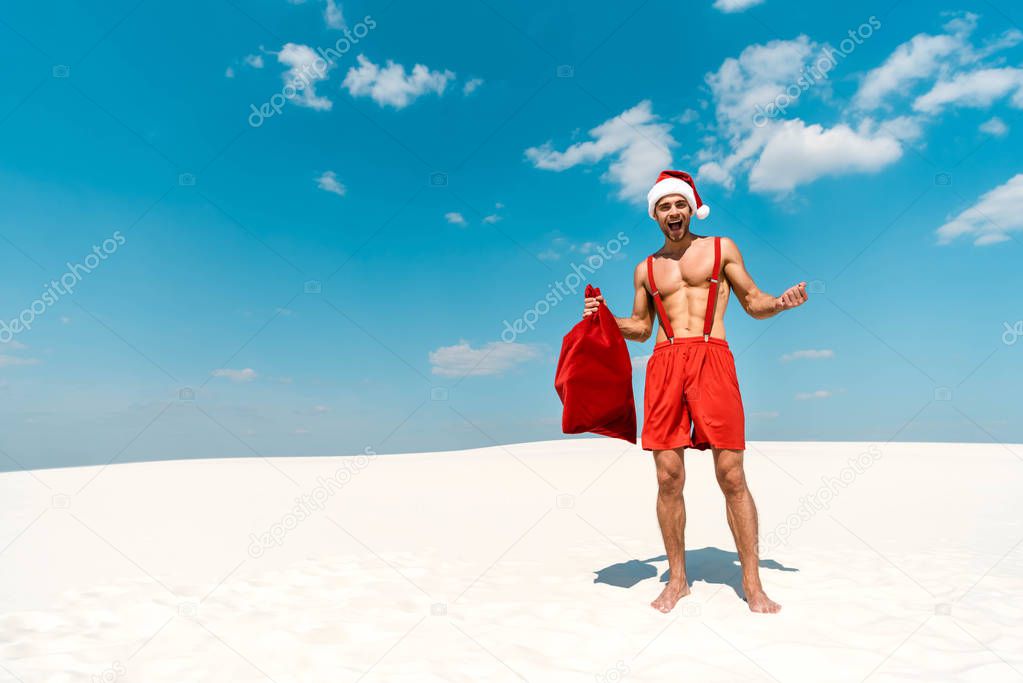 shocked and sexy man in santa hat holding santa sack on beach in Maldives 