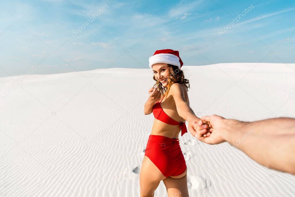 cropped view of boyfriend holding hand of sexy girlfriend in santa hat on beach in Maldives 