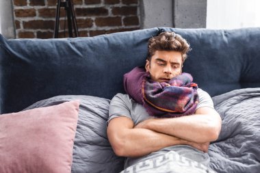 sick and handsome man in scarf lying in bed  clipart