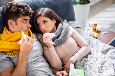 sick girlfriend and boyfriend holding napkins and looking at each other in apartment  clipart
