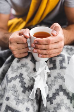 Apartman dairesinde elinde çay tutan adamın kırpılmış görüntüsü. 