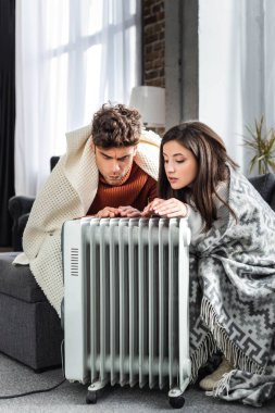 attractive girlfriend and boyfriend covered with blankest warming up near heater  clipart