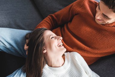 high angle view of attractive girlfriend in sweater smiling and lying on knees of boyfriend  clipart
