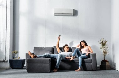 handsome boyfriend switching on air conditioner and looking at smiling girlfriend clipart