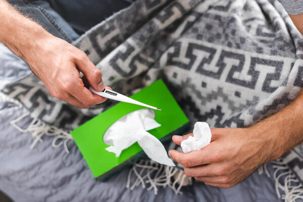 cropped view of sick boyfriend holding thermometer and napkin