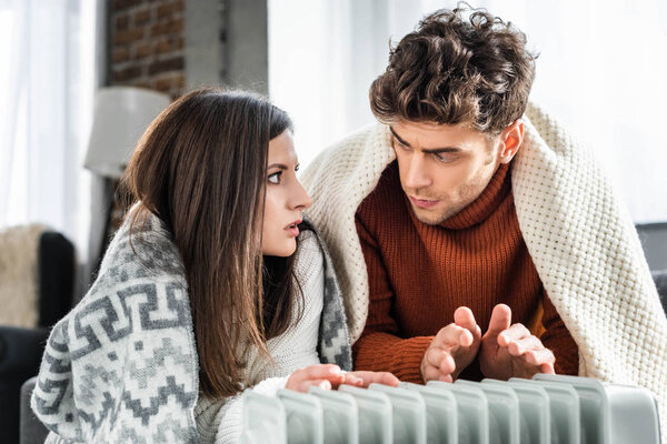 attractive girlfriend and boyfriend covered with blankest warming up near heater 